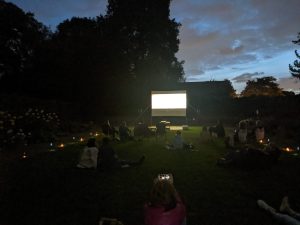 A bright screen, lit up while showing a film, against a darker sky. In the gardens behind Charlton House with an evening showing of Running for Good.