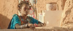 A still from the film Timbuktu showing a woman in a blue dress looking pensive