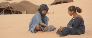 A still from the film Timbuktu showing two children, a boy and a girl, sitting and playing a game in the sand